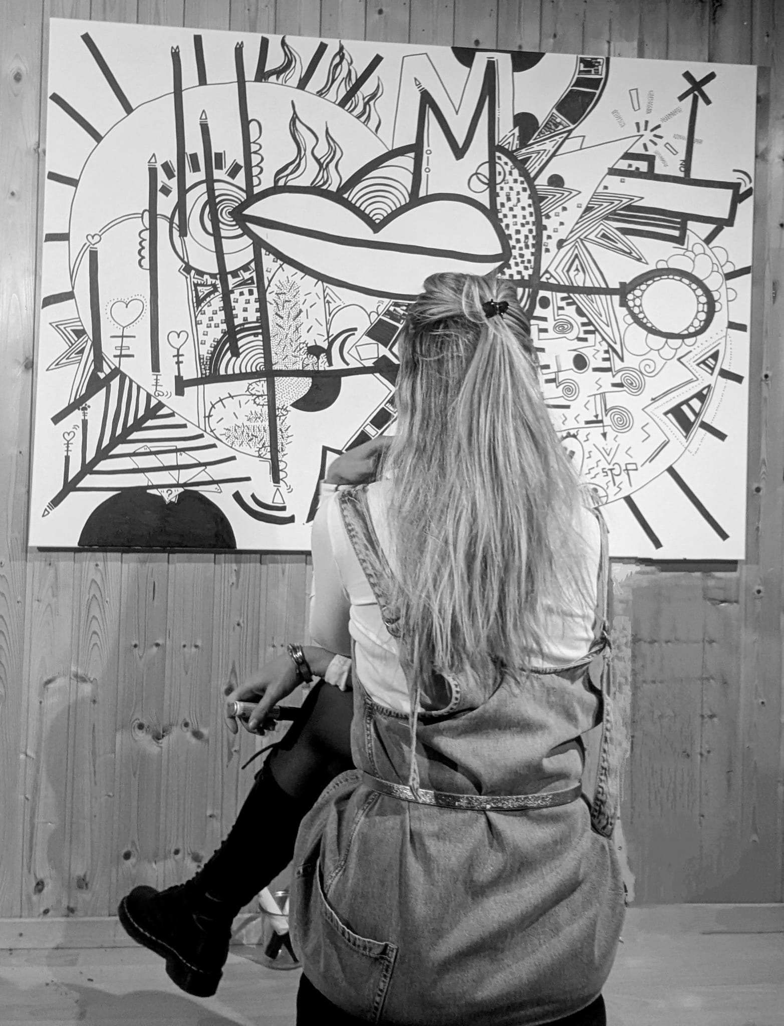 L'artiste de dos, assise face à l'une de ses toiles en cours d'exposition